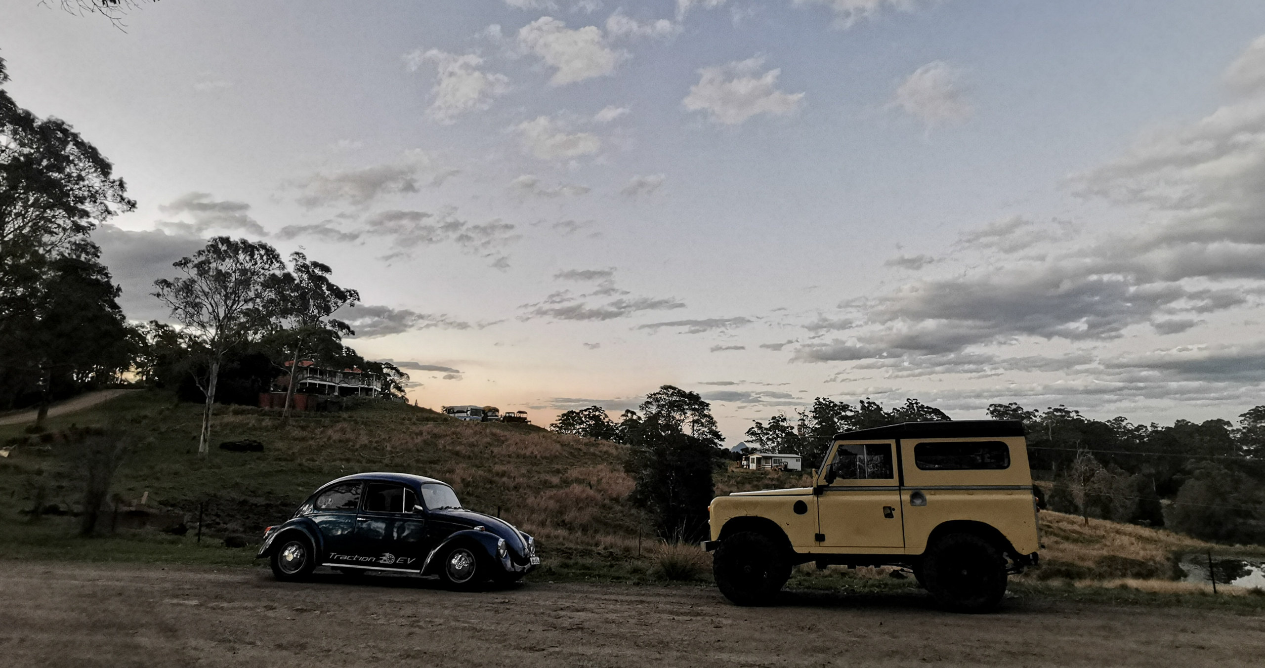 The electric 1973 Series 2 Land Rover and the 1968 EV Beetle facing off at dusk.